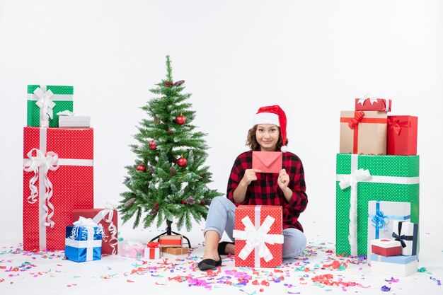 Front view of young woman sitting around presents holding envelop on white wall