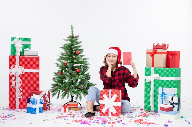 Front view of young woman sitting around presents holding envelop on white wall