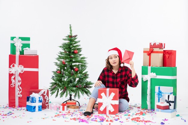 Front view of young woman sitting around presents holding envelop on white wall