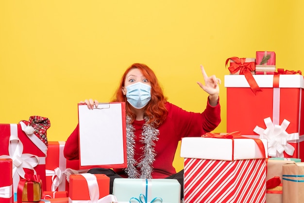 Free photo front view of young woman sitting around presents in mask with file note on the yellow wall