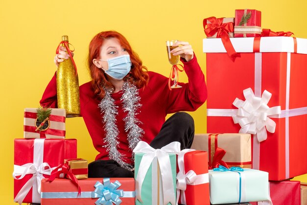 クリスマスの周りに座っている若い女性の正面図黄色の壁にシャンパンとマスクでプレゼント