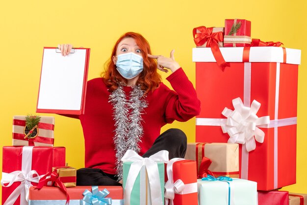 Вид спереди молодая женщина, сидящая вокруг рождественских подарков с файловой заметкой о вирусе желтых эмоций, цвет covid- новый год