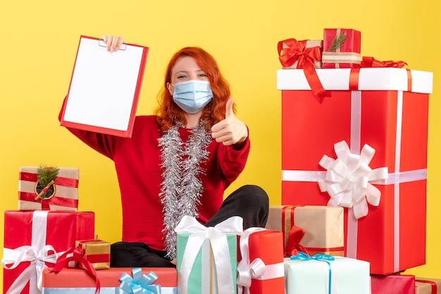 Front view young woman sitting around xmas presents with file note on a yellow