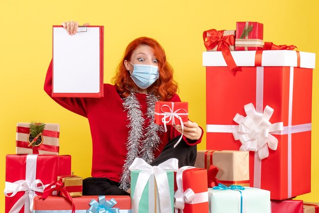 Front view young woman sitting around xmas presents with file note on the yellow