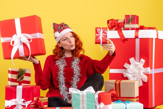 Front view of young woman sitting around xmas presents on a yellow wall