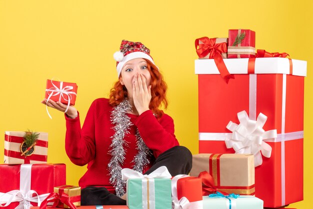 Front view of young woman sitting around xmas presents on a yellow wall