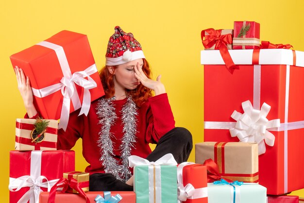 Front view of young woman sitting around xmas presents on yellow wall