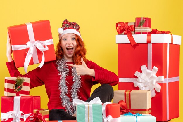 Front view of young woman sitting around xmas presents on yellow wall