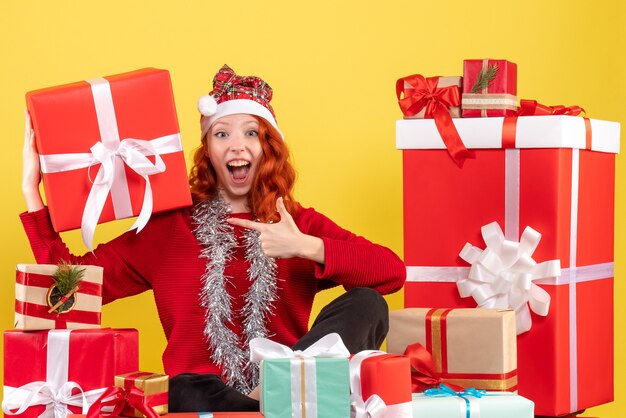 크리스마스 주위에 앉아있는 젊은 여자의 전면보기 노란색 벽에 선물