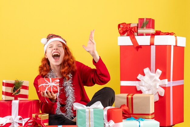 Front view of young woman sitting around xmas presents on yellow wall