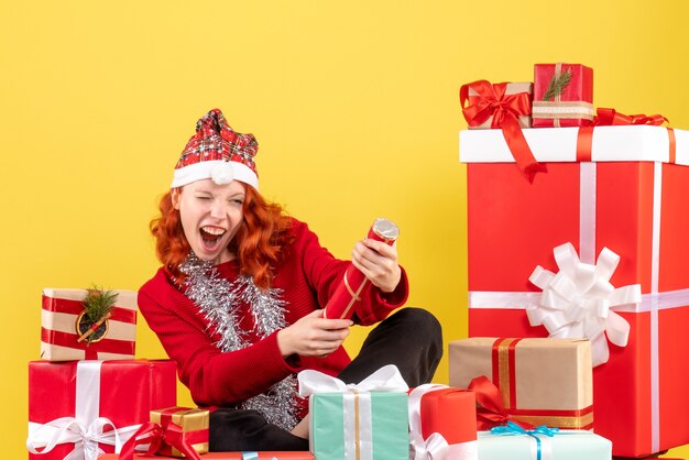 크리스마스 주위에 앉아있는 젊은 여자의 전면보기 노란색 벽에 선물