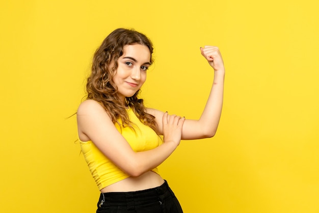 Front view of young woman smiling and flexing on yellow wall