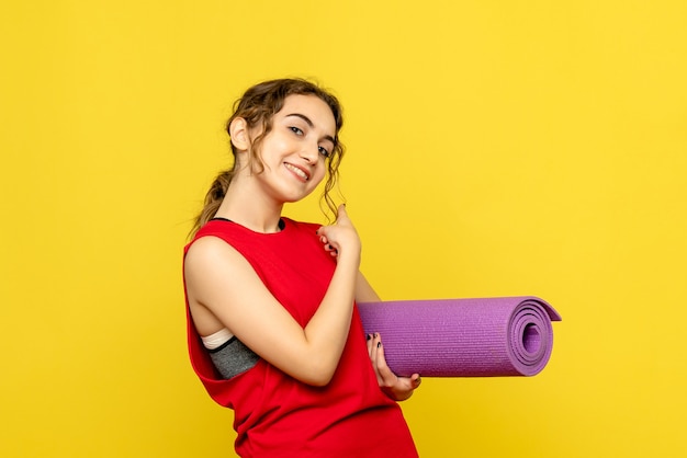 Вид спереди молодой женщины, улыбающейся с фиолетовым ковром на желтой стене