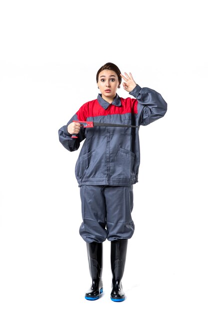 front view of young woman in special uniform holding hacksaw on white wall