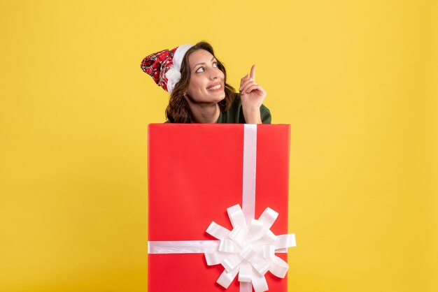 Front view of young woman standing inside box on yellow wall