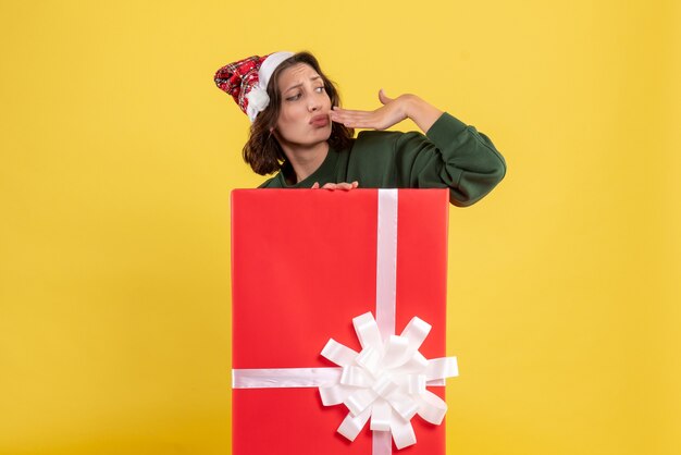 Front view of young woman standing inside box on yellow wall