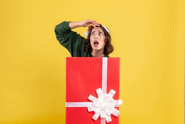 Вид спереди молодой женщины, стоящей внутри подарочной коробки на желтой стене