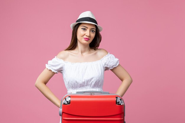 ピンクの壁の休暇の飛行機の航海夏の感情旅行で赤い休暇バッグと立っている正面図若い女性
