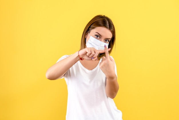 黄色の壁に滅菌マスクで若い女性の正面図