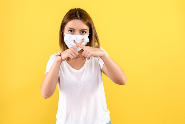 Front view of young woman in sterile mask on a yellow wall