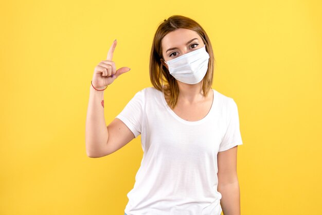 Front view of young woman in sterile mask on a yellow wall