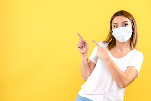 Front view of young woman in sterile mask on a yellow wall