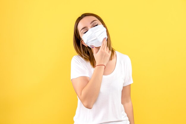 Front view of young woman in sterile mask on yellow wall