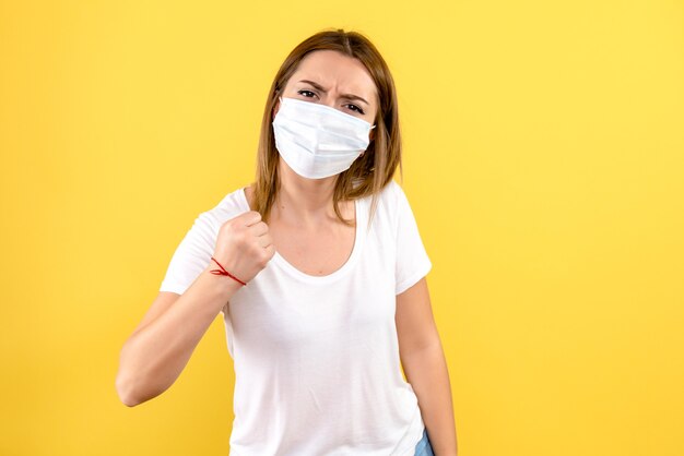 Front view of young woman in sterile mask on yellow wall