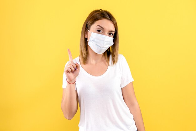 Front view of young woman in sterile mask on yellow wall