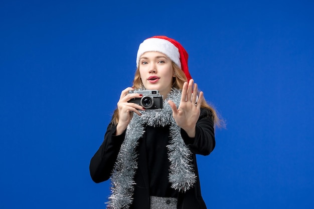 Front view of young woman taking photo with camera on a blue wall