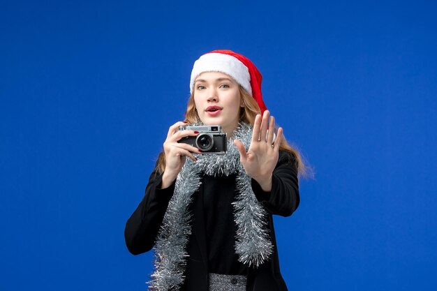 Front view of young woman taking photo with camera on a blue wall