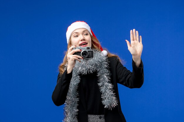 Front view of young woman taking photo with camera on a blue wall