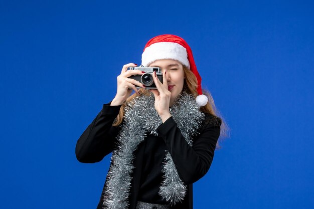 Вид спереди молодой женщины, делающей фото с камерой на синей стене