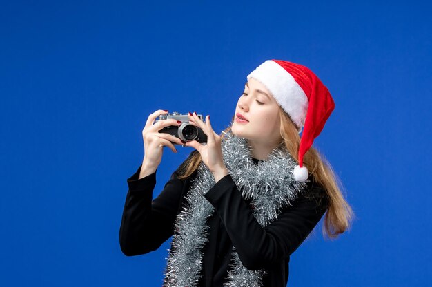 Vista frontale della giovane donna che prende foto con la macchina fotografica sulla parete blu