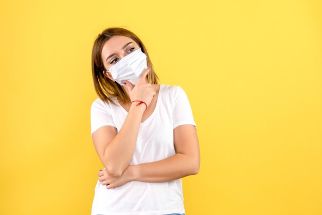 Front view of young woman thinking in mask on yellow wall