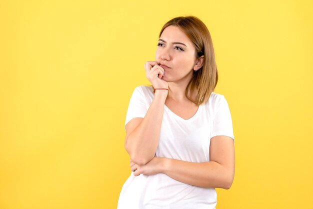 Vista frontale della giovane donna che pensa sulla parete gialla