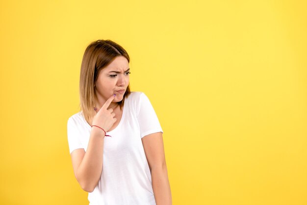 Front view of young woman thinking on yellow wall