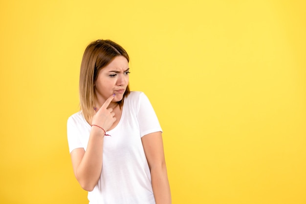 Front view of young woman thinking on yellow wall