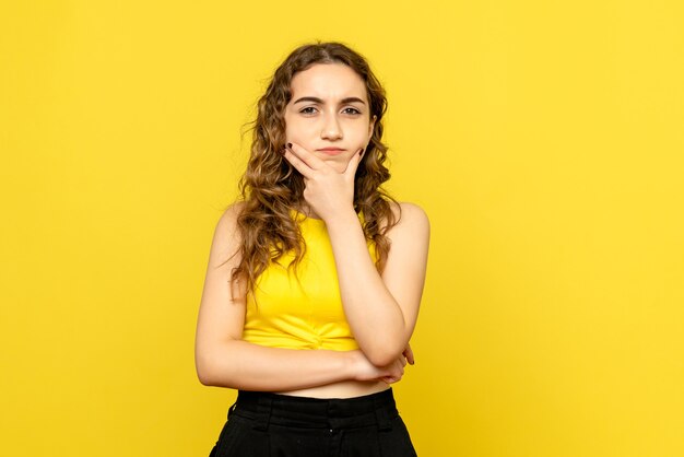 Front view of young woman thinking on yellow wall