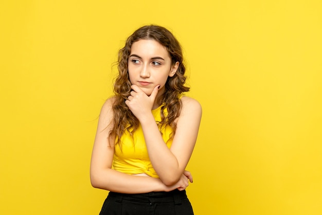 Front view of young woman thinking on yellow wall
