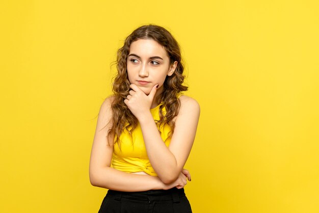 Front view of young woman thinking on yellow wall