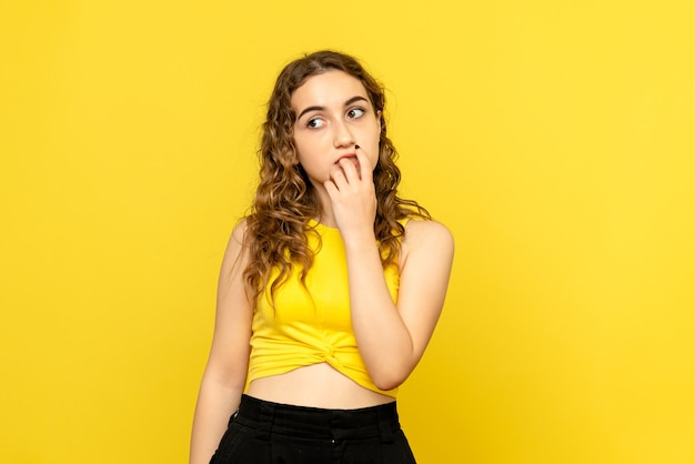 Front view of young woman thinking on yellow wall