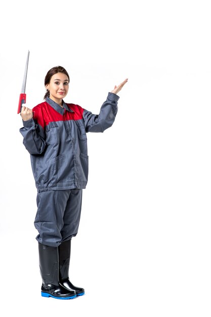 front view of young woman in uniform holding hacksaw on white wall