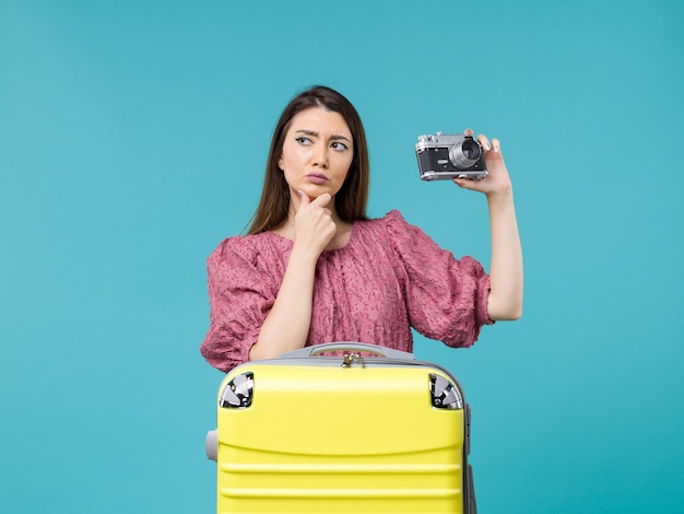 Front view young woman in vacation holding photo camera and thinking on blue background journey sea trip woman abroad vacation