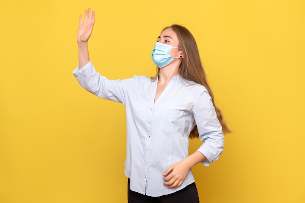 Front view of young woman waving on yellow wall