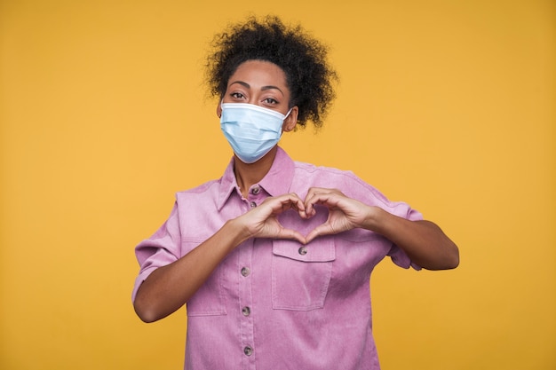 Free photo front view of a young woman wearing a medical mask and showing a heart with her hands