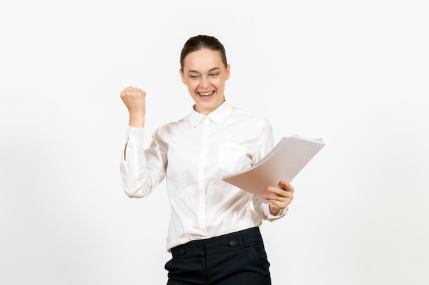 Вид спереди молодая женщина в белой блузке, держащая документы и улыбающаяся на белом фоне, женская работа, эмоции, чувство офиса