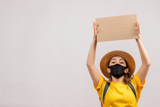 Vista frontale giovane donna con zaino che indossa una maschera nera con cartone sopra la testa