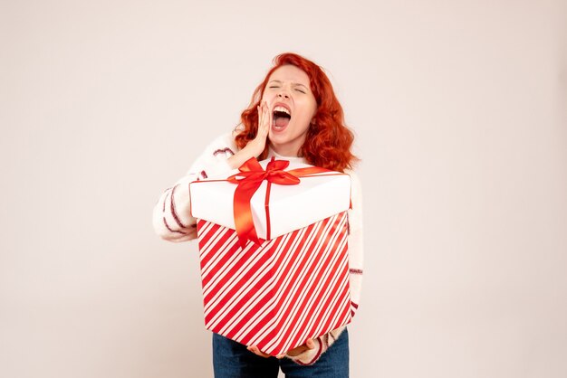 Front view of young woman with big present screaming on white wall