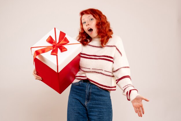 Front view of young woman with big present on white wall